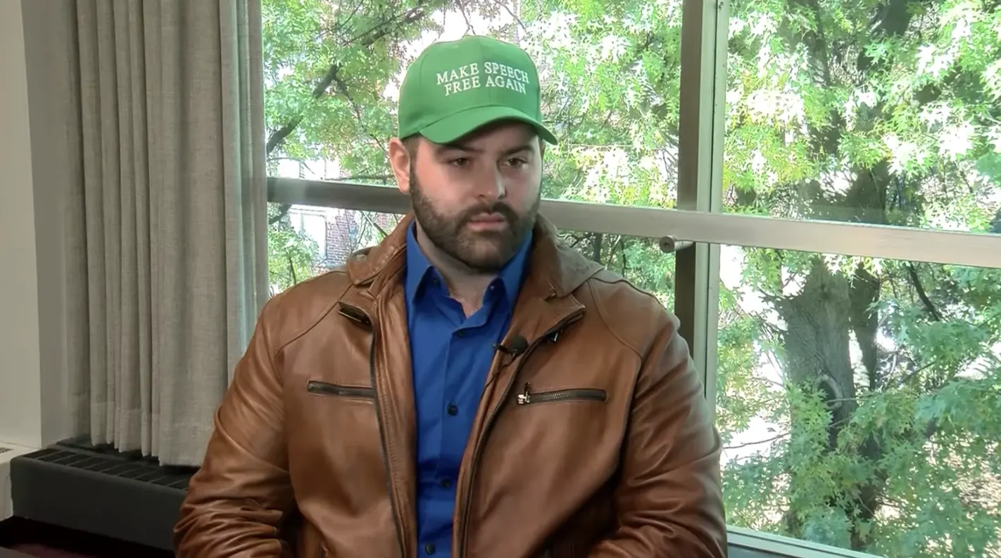 Man sits in a Make Speech Free Again green hat