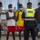 A police officer tells migrants and asylum-seekers to stop playing soccer due to coronavirus restrictions on contact sports in Gran Canaria island, Spain, Tuesday, Aug. 18, 2020. Image by Emilio Morenatti/AP Photo. Spain, 2020.