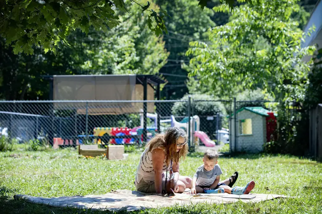 Bell’s School teacher Angela Mehaffey reads a book with Elliot Fink, 2, on a blanket outside the Fletcher preschool June 22. Image by Angeli Wright/Asheville Citizen Times/North Carolina News Collaborative. United States, 2020.