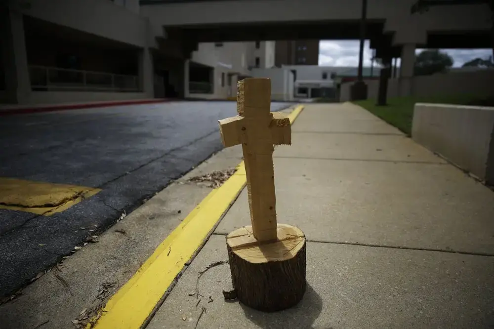 A wooden cross made from a tree stump, known by some locals as a symbol of hope, sits outside of Phoebe Putney Memorial hospital on Monday, April 20, 2020, in Albany, Ga. The patients were very sick. Some died within hours. Some died on the way, in the back of ambulances. The region is predominantly black, but even so, African Americans died disproportionally, said Phoebe Putney Memorial's chief executive officer Scott Steiner. Image by Brynn Anderson / AP Photo. United States, 2020.