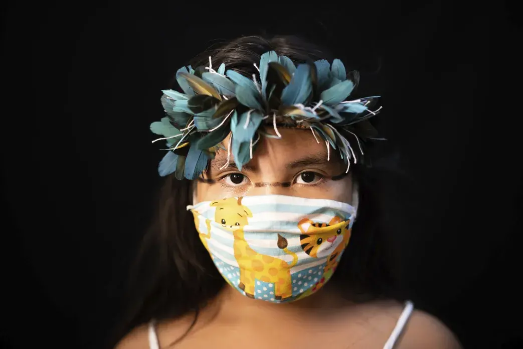 Iasmin, 8, of the Sateré Mawé indigenous ethnic group, poses for a portrait wearing the traditional dress of her tribe and a face mask amid the spread of the new coronavirus in Manaus, Brazil, Wednesday, May 27, 2020. Image by Felipe Dana / AP Photo. Brazil, 2020.