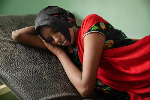 In this July 26, 2019 photo, Fadya Mohammed, a migrant from Ethiopia, lays on a gurney after disembarking from a boat and feeling sick from the sea, at the Ras al-Ara Hospital, Lahj, Yemen. In Djibouti, her and her sister were held by traffickers, who beat them and ordered them to ask their parents to send money for their release. The parents had to borrow money from neighbors to secure their daughter's release. Image by Nariman El-Mofty / AP Photo. Yemen, 2019.