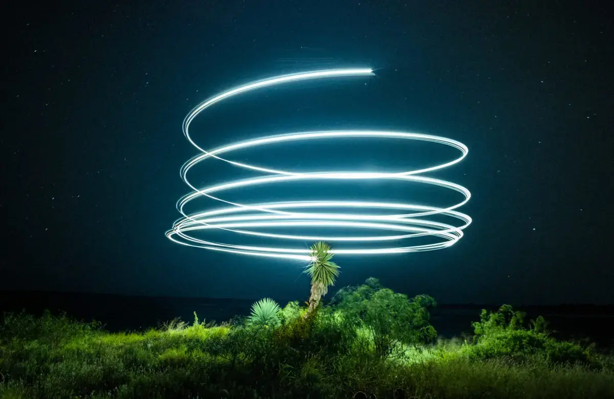 a light spiral above a tree illuminated under a black sky