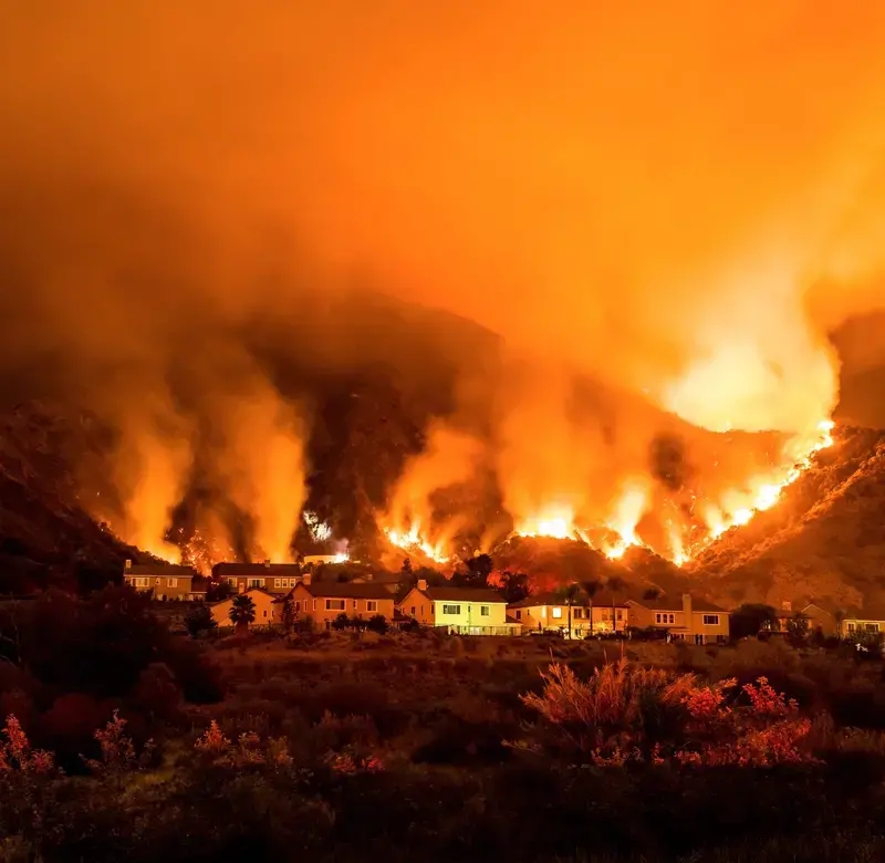 wildfires rage in the hills behind a set of houses in the hills