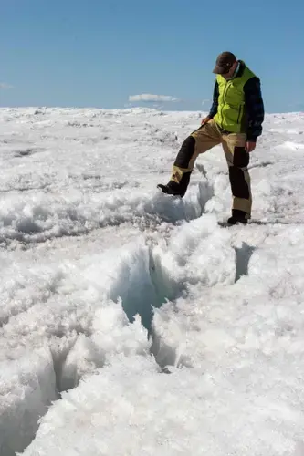 University of Montana glaciologist Joel Harper steps over a deep crack in the ice sheet called a crevasse. Image by Amy Martin. Greenland, 2018.