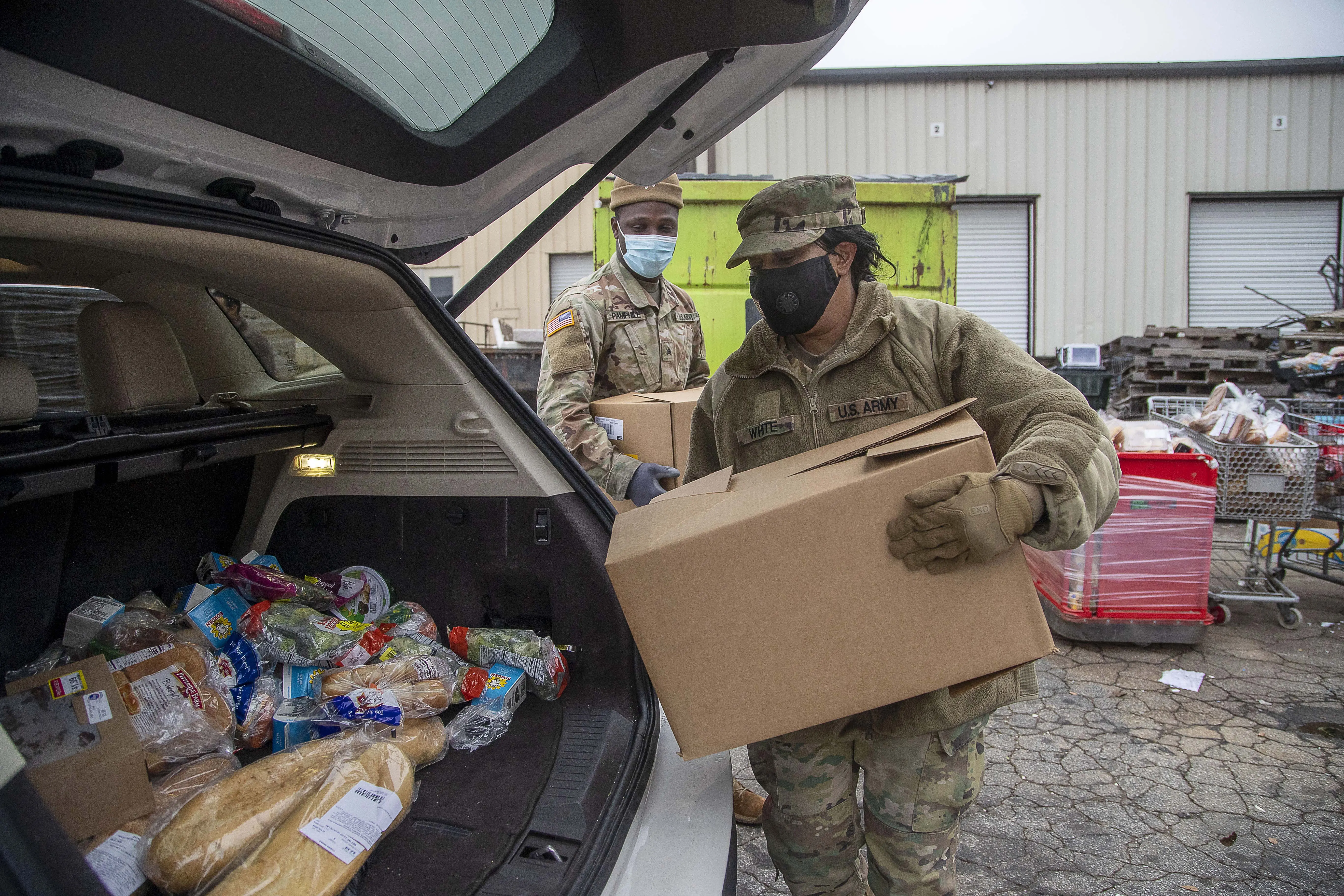 People dressed in military uniforms and wearing masks load boxes into the trunk of a car.