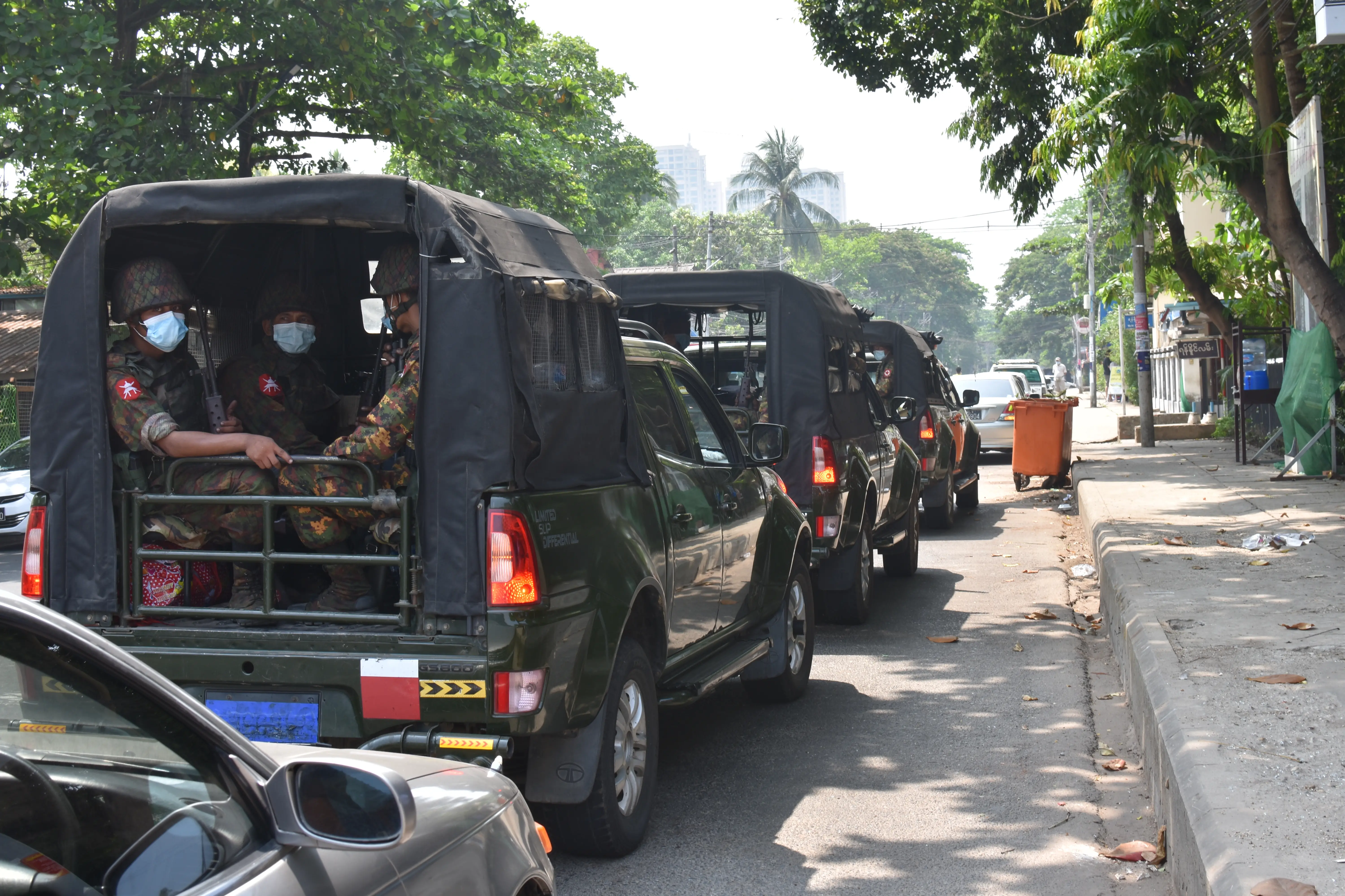 Soldiers wearing medical masks can be seen from the back of a truck in a convoy.