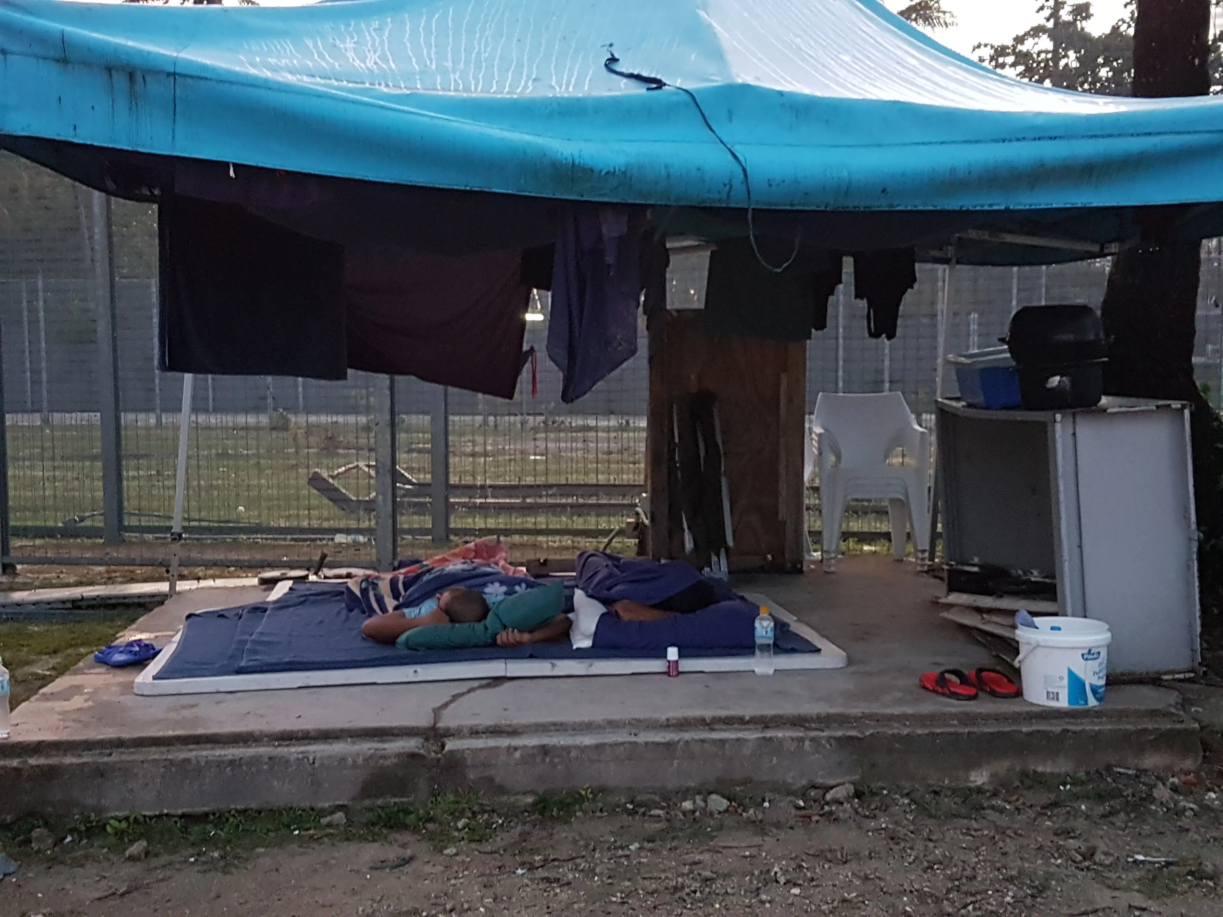 refugees sleep in the open beneath a tent