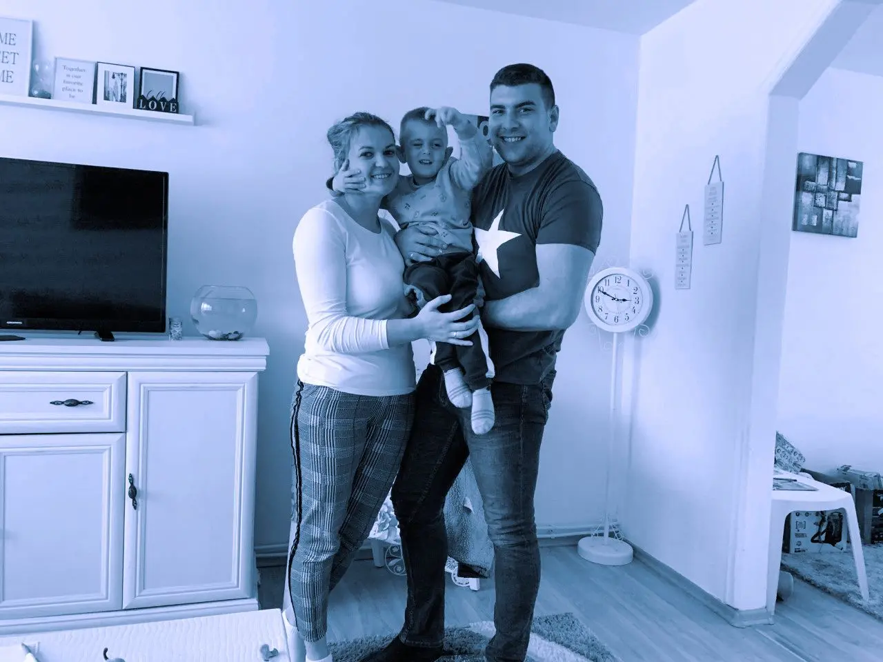 A woman and man hold a child in a living room.