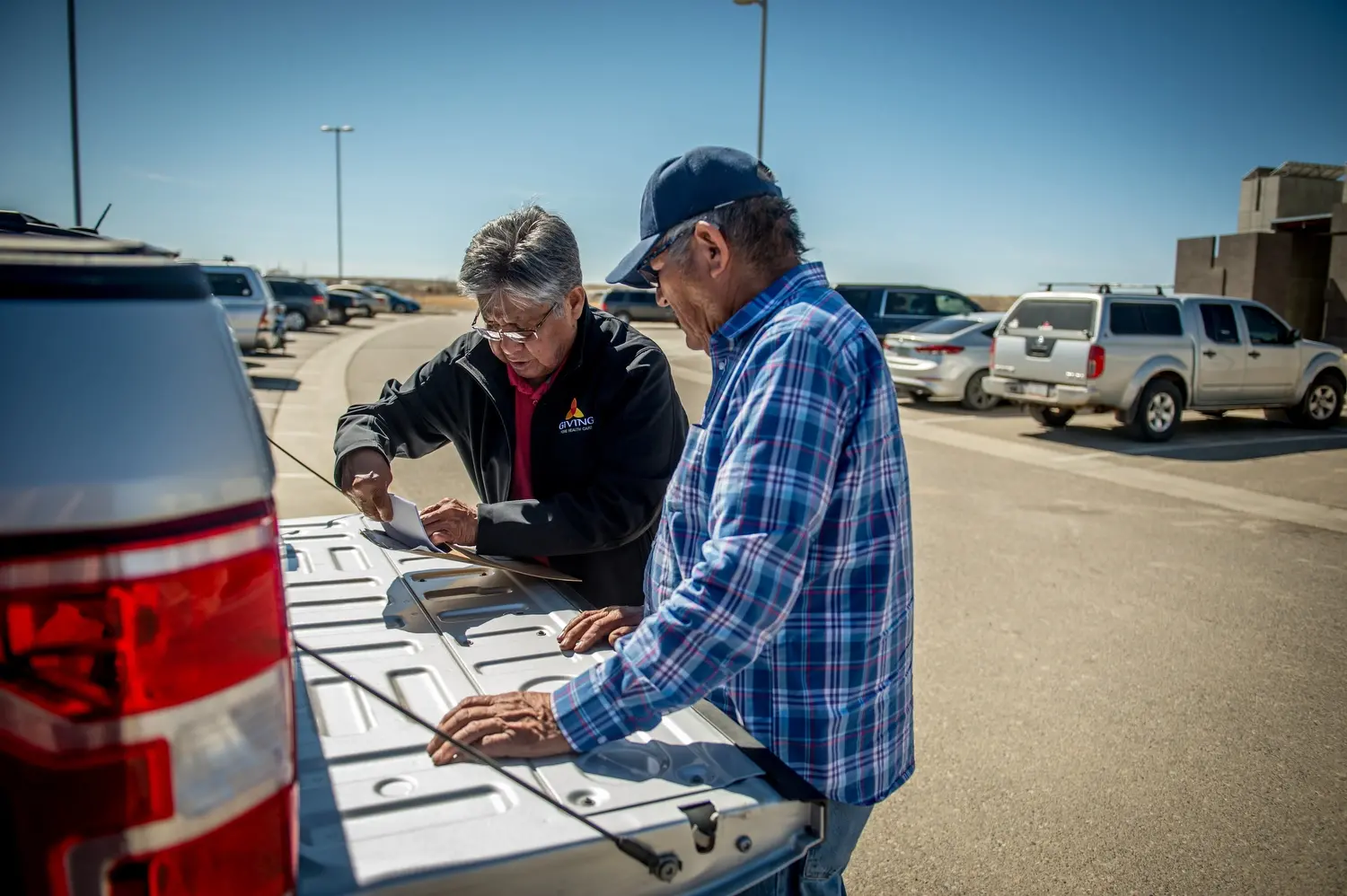 Phil Harrison, left, is pictured assisting a former miner in filing a claim through the Radiation Exposure Compensation Act in a parking lot. Image by Mary F. Calvert. United States, 2020.