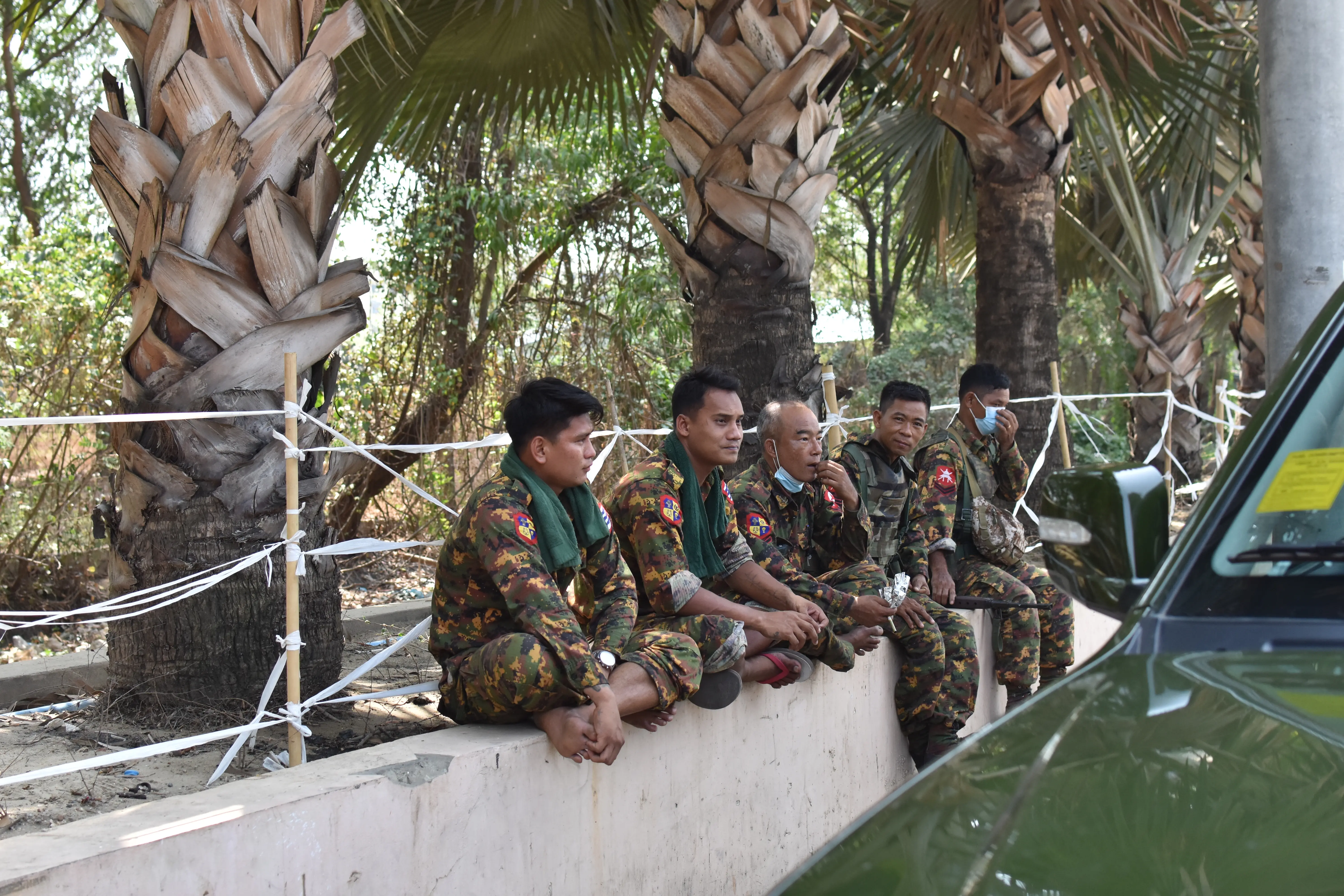Soldiers sit on a wall in front of palm trees.